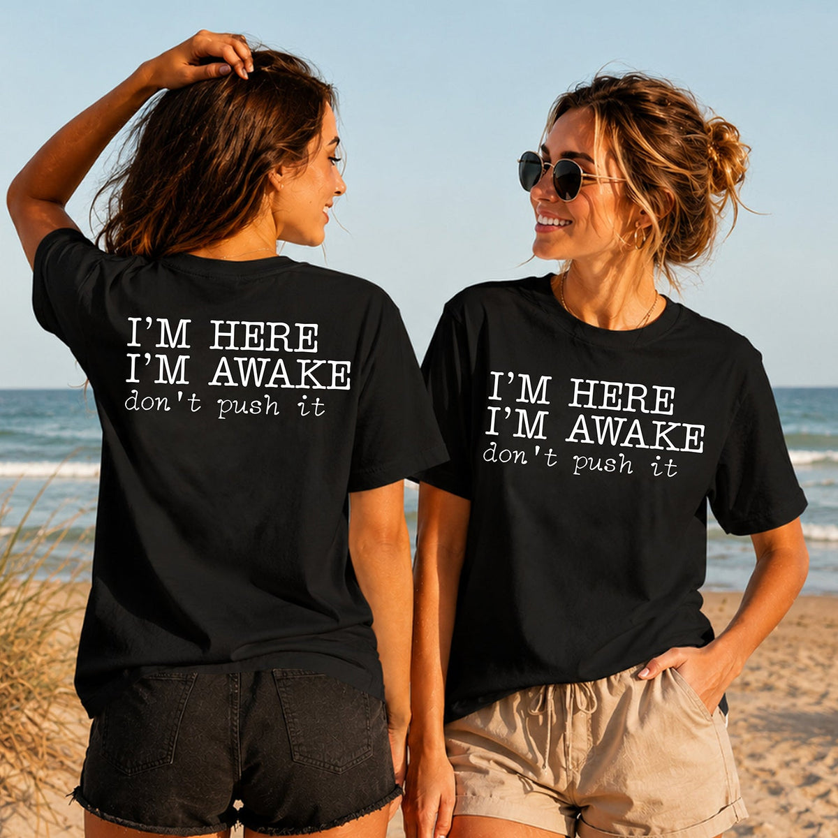 I'm Here I'm Awake - Women's T-Shirt in black, showing alternative back and front print placements on the beach