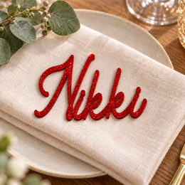 Nikki in Bentory Authes font, Bright Red Glitter Acrylic personalised guest name on an ivory napkin.